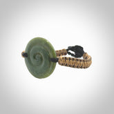 This picture shows a hand carved jade contemporary koru bracelet. It is a deep green Jade. It is a wonderful, delicate piece of jewellery. The cord is hand plaited and fixed with a black jade toggle. This bracelet was carved for us by Sheree Warren. Delivery is free worldwide.